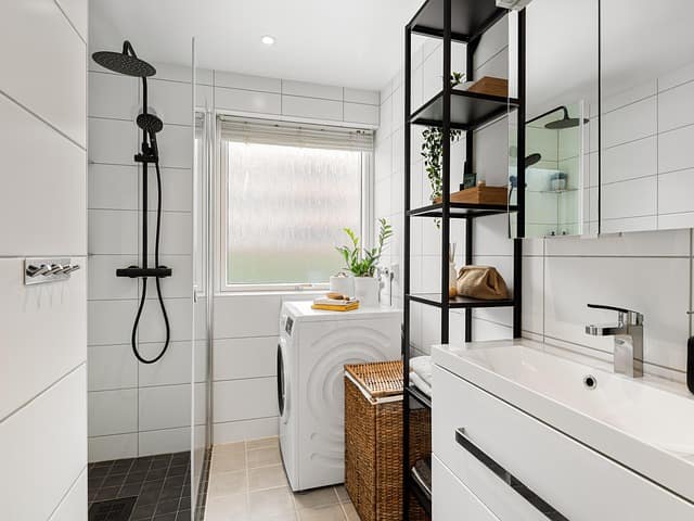 Clean white bathroom and laundry room combo with shower, sink, and washer in Durham NC home
